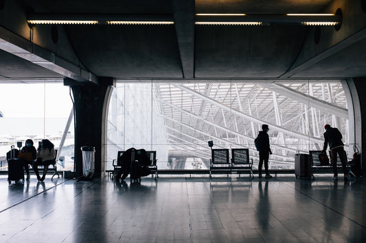 Travellers waiting with rolling suitcases beside large airport terminal windows