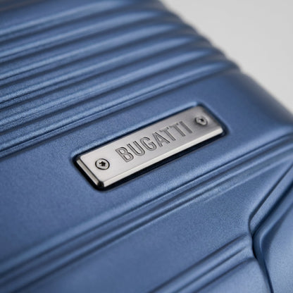 Macro detail of the Bugatti Nashville navy luggage showing a brushed metal logo plate on a textured hardshell PET surface.