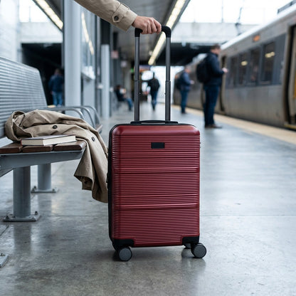 Deep red Bugatti Brussels hardside carry-on luggage held at a train station platform.