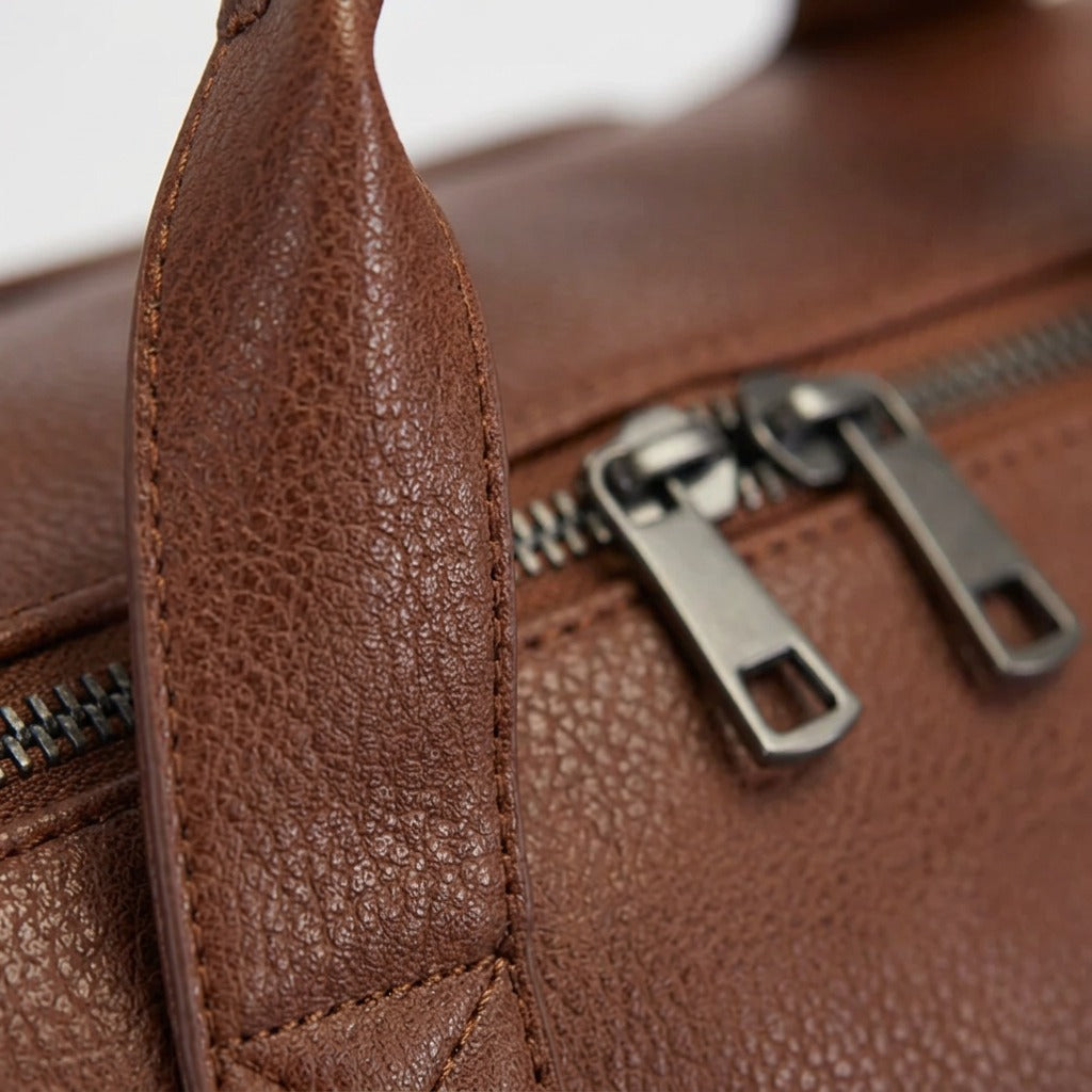 Macro detail of the Bugatti Palermo Duffle Bag showing cognac vegan leather texture and metal zippers.