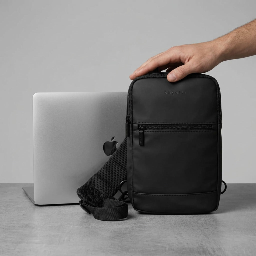 Scale comparison of the black matte Bugatti Mile End Sling Bag next to a laptop for size reference.