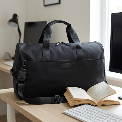 Black Bugatti Reborn convertible duffle bag on a desk next to an open book and computer monitor.