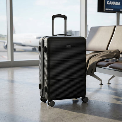Black Bugatti Brussels 24-inch hard shell suitcase standing in a bright airport terminal.