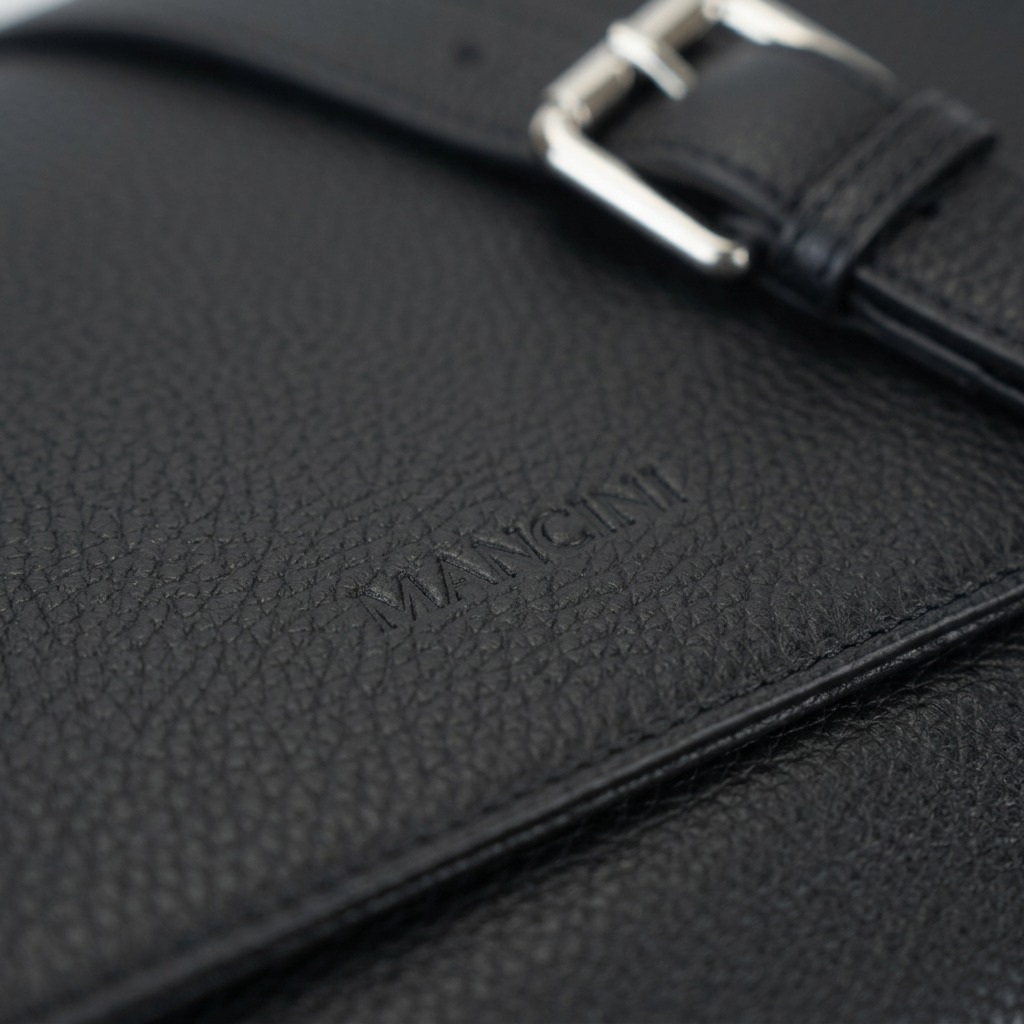 Macro lens image showing the detailed grain of the Mancini Alison handbag's pebble-texture leather and precise logo embossing.