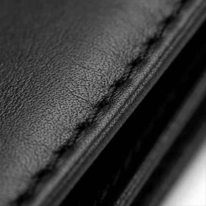 Macro photograph of natural grain leather texture and precise stitching on the black Mancini wallet.
